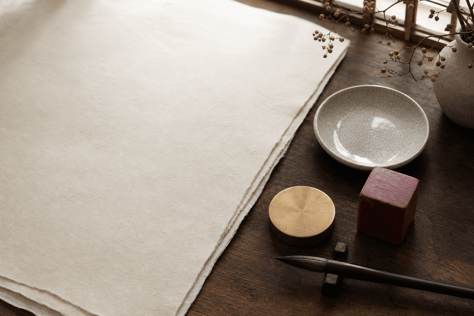 Porcelain dish, blank handmade paper, brass disc, red seal, and brush on a wooden table